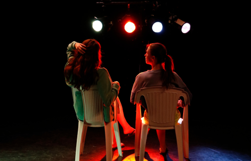 Photo de répétition de Miss Camping, avec deux actrices sur des chaises en plastique, de dos
