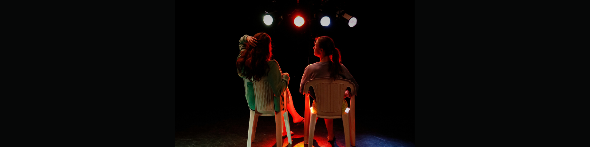 Photo de répétition de Miss Camping, avec deux actrices sur des chaises en plastique, de dos