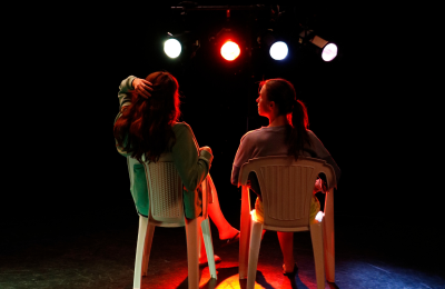 Photo de répétition de Miss Camping, avec deux actrices sur des chaises en plastique, de dos